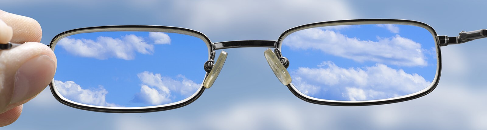 Blick auf die Wolken am Himmel durch eine hochgehaltene Brille.