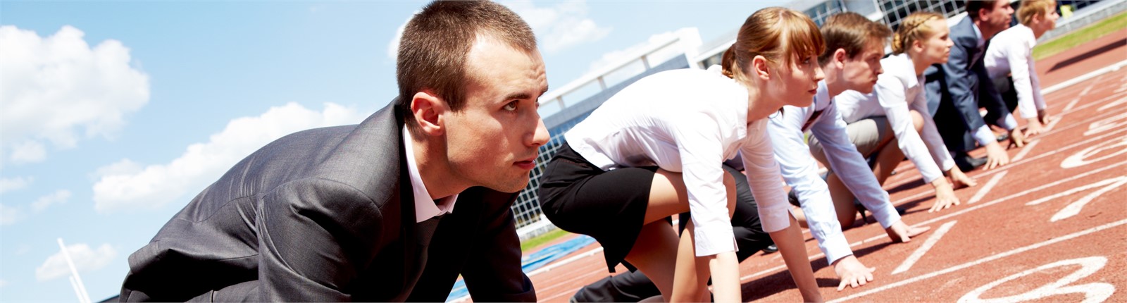 Männer und Frauen im Business-Anzug in einem Leichtathletikstadion mit dem Fuss im Startpflock