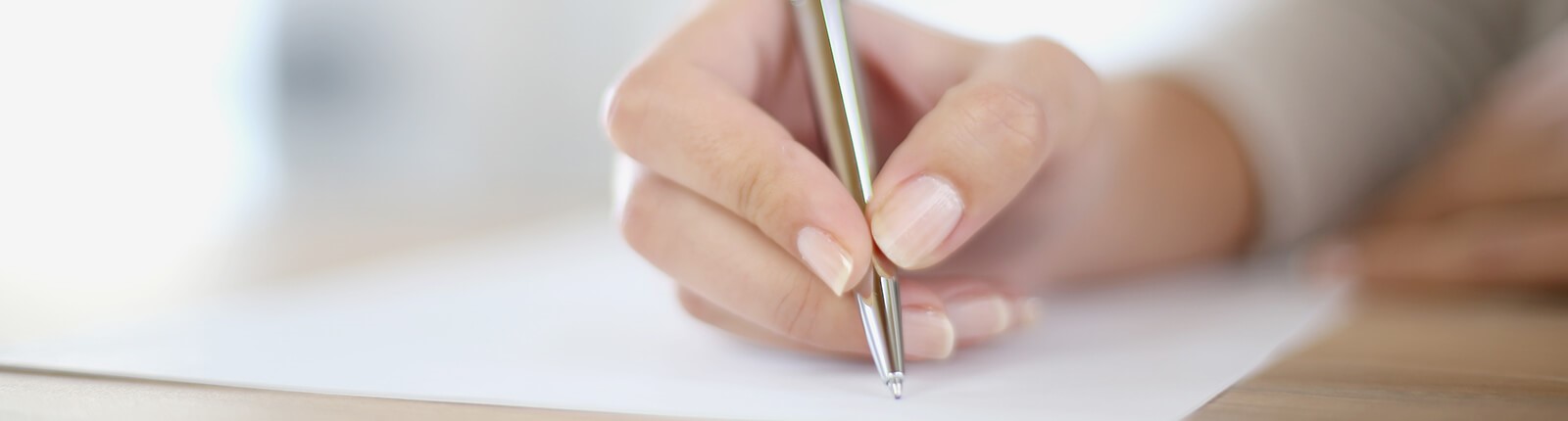 Eine Frau schreibt mit einem silberfarbenen Stift einen Brief.